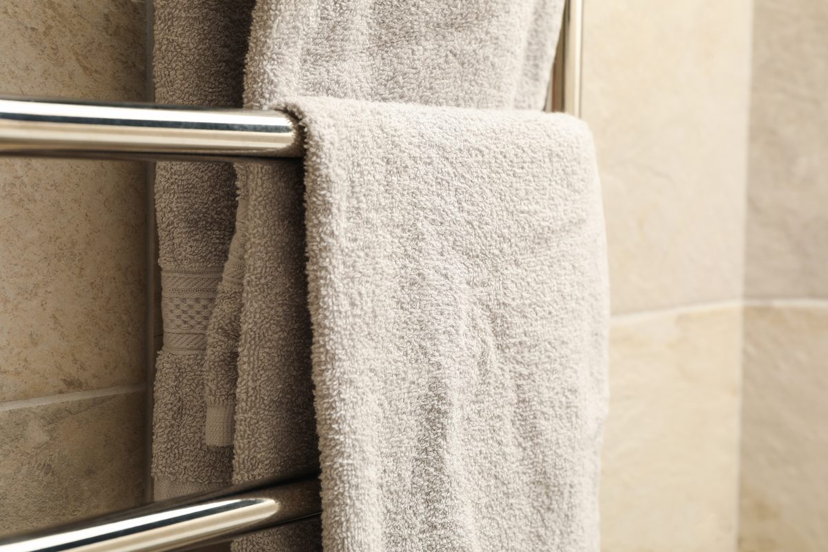 Folded towels hanging on a chrome heated towel rail against a tiled bathroom wall